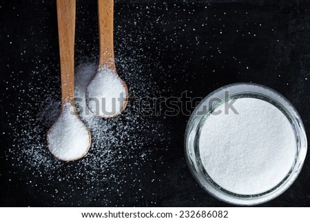 sugar in wooden spoons and glass jar on black background