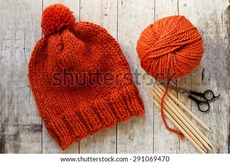 wool orange hat, knitting needles and yarn on wooden background