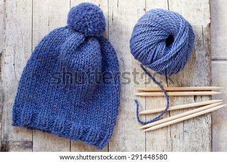 wool blue hat, knitting needles and yarn on wooden background