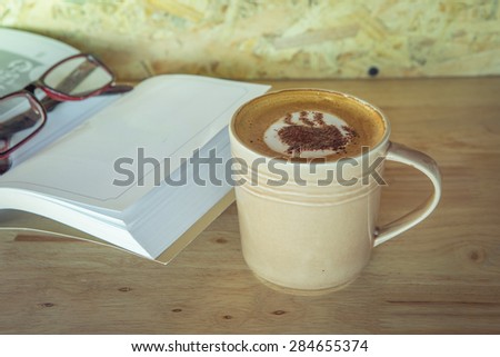 Cup of coffee with book and grass on table