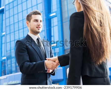 Business partners shaking hands, standing in front of his office.