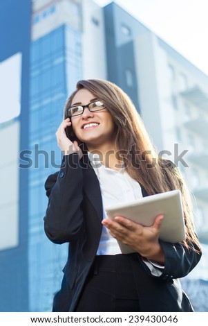 Successful businesswoman or entrepreneur using a digital tablet computer and talking on cellphone standing in front of his office.