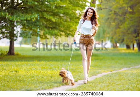 Beautiful girl walking in the park with a small dog and smiling