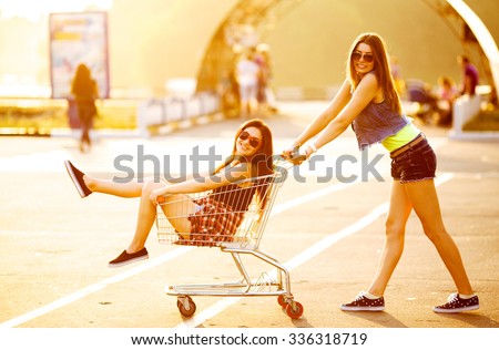 Girlfriends laughing. Girlfriends ride in a cart at the supermarket on the streets of the city.