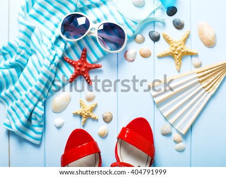 Summer women\'s accessories: sunglasses, red shoes, dress on blue wood background.
