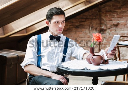 Man reading a brochure in cafe. Rose on the table.