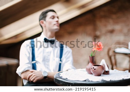 Man poses in cafe with rose on the table.