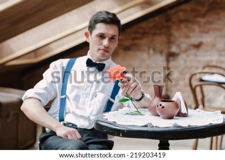 Man poses with rose in cafe.