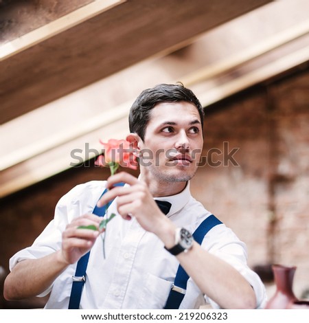 Man poses with rose in cafe.