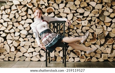 Funny portrait of pretty girl in front of the pile of wood, classic dress. Wooden pile background.