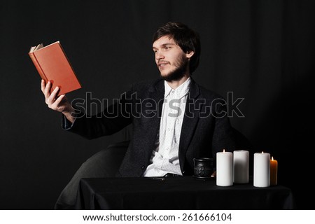 Young man reading a book by the table. Coffee, candles and enigmatic atmosphere.