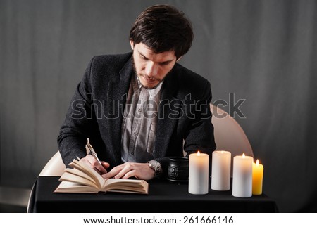Young man writing notes in the notebook. Coffee, candles and enigmatic atmosphere.
