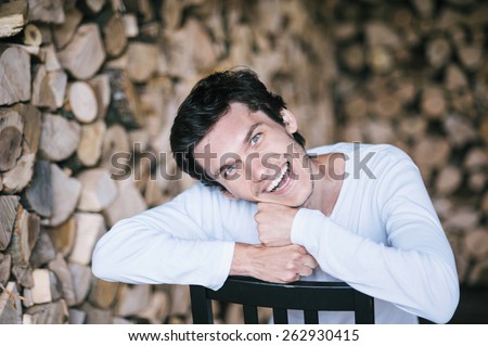 Young man sitting and leaning on the back of the chair. Fancy face expression. Firewood background.