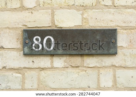 80 Eighty engraved on stone plate mounted on brick wall closeup