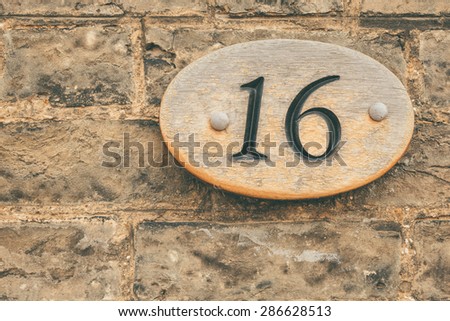 Wooden plate number 16 sixteen on brick wall conceptual image closeup