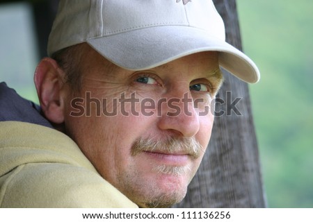 Head of friendly, handsome middle-aged man wearing a baseball cap looking sidewards into camera.