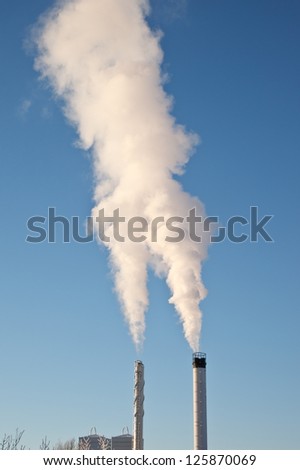 A factory chimney with rising smoke against a blue sky