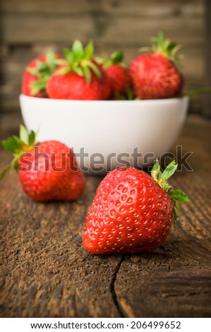 white china bowl filled with succulent fresh ripe red strawberries on an old wooden textured table top