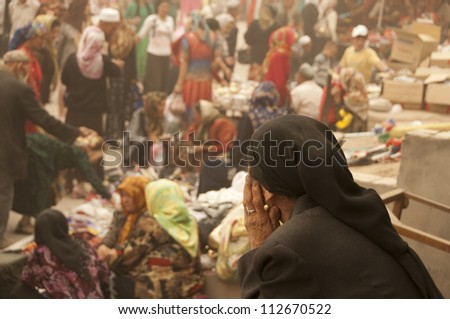 Old woman sat staring at people shopping at a market in Kashgar, China