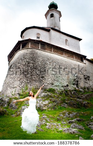 Happy bride jumping in her wedding dress, in front of medieval castle