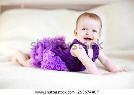 Laughing baby girl in purple dress on white bed
