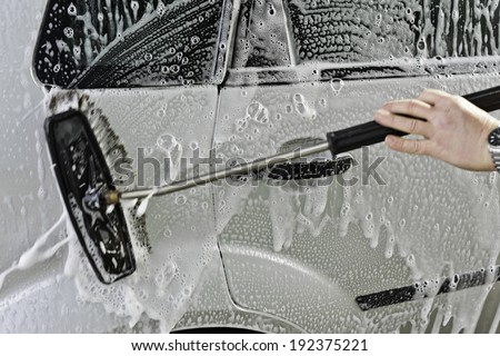 Car wash with water and scrubbing brush in Action - Focus is on the car