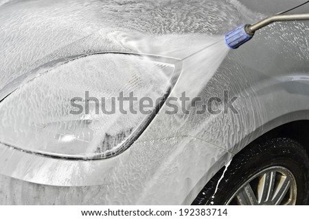 Car wash himself with high pressure cleaners in motion - focus is on the car