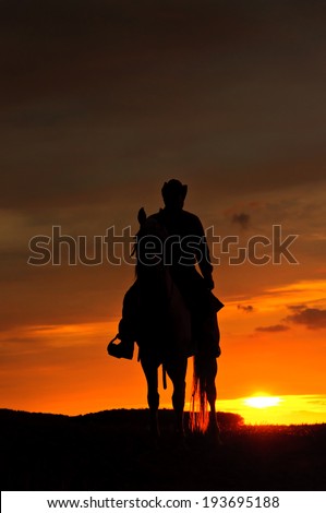Cowboy riding his horse towards the sun