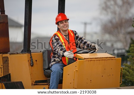 Smiling road construction worker behind construction roller\'s wheel.
