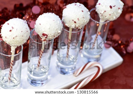 Holiday candy cane cake pops in a row of shot glasses on white plate with candy canes