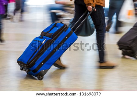 Woman walking quickly pulling blue luggage in busy airport
