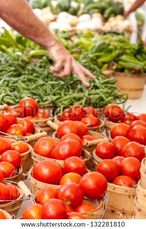 Male hand picking fresh home grown organic tomatoes in bushel baskets on display at local farmers market