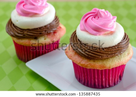 2 neapolitan frosted cupcakes sitting on white plate with green diamond background