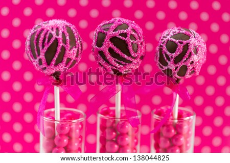 Pink swirled chocolate cake pops with light bright pink polka dot background standing in candy filled shot glasses