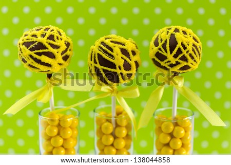 Yellow swirled chocolate cake pops with lime green polka dot background standing in candy filled shot glasses