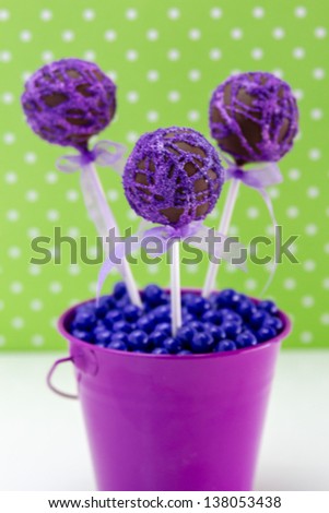 Chocolate cake pops with purple swirl glitter sugar decorations against green polka dot background, portrait orientation