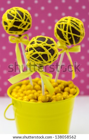 Chocolate cake pops with yellow swirl glitter sugar decorations against pink polka dot background, portrait orientation