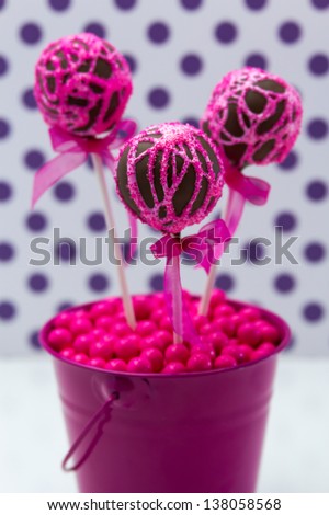 Chocolate cake pops with pink swirl glitter sugar decorations against white background with purple polka dots, portrait orientation
