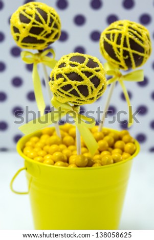 Chocolate cake pops with yellow swirl glitter sugar decorations against white background with purple polka dots, portrait orientation