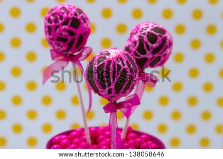 Chocolate cake pops with pink swirl glitter sugar decorations against white background with yellow polka dots