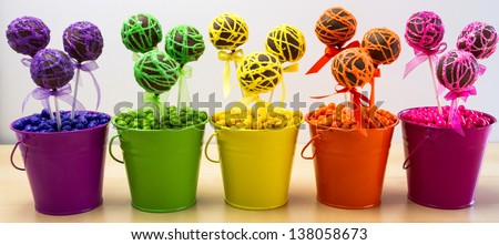 Line of rainbow colored chocolate cake pops in colored buckets and colored candy balls