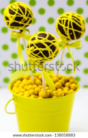 Chocolate cake pops with yellow swirl glitter sugar decorations against white background with green polka dots, portrait orientation