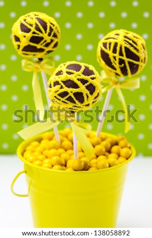Chocolate cake pops with yellow swirl glitter sugar decorations against green polka dot background, portrait orientation