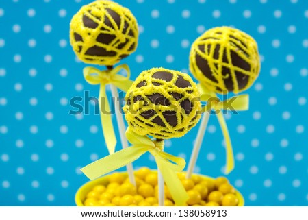 Chocolate cake pops with yellow swirl glitter sugar decorations against blue polka dot background