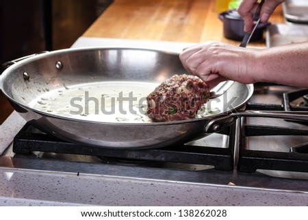 Female chef hand pushing raw hamburger into hot stainless steel pan to cook burger