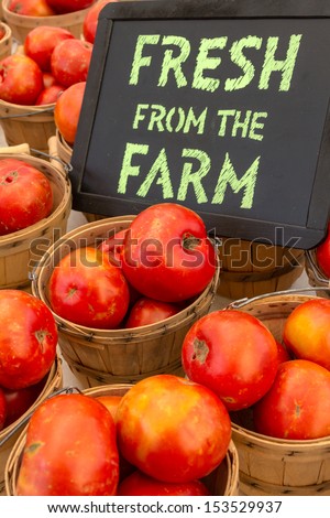Organically grown red tomatoes in baskets for sale at local farmer market with chalkboard sign
