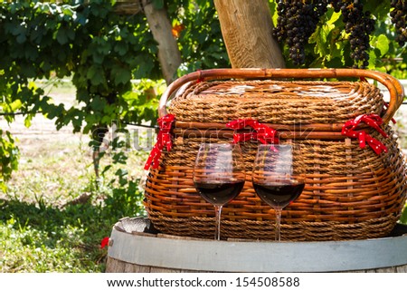 Close up of picnic scene in vineyard with wicker basket and 2 glasses of red wine sitting on wine barrel