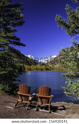 Pair of Adirondack Chairs sitting by mountain lake with snow covered peaks in distance