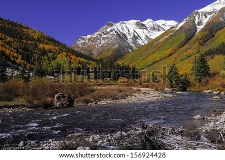 Changing Aspens trees on fall afternoon along mountain stream with snow covered peaks