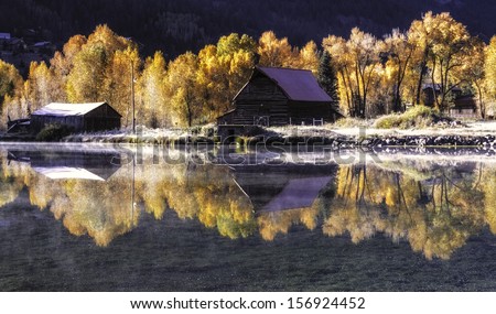 Fall scene of an abandoned ranch reflected in a pond with changing fall trees on a frosty cold morning